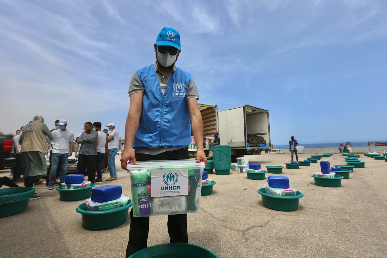 UNHCR aid worker distributing supply kits in an outdoor setting illustrating foreign aid distribution efforts